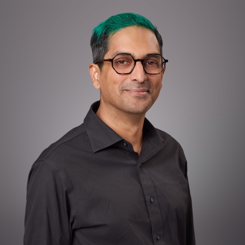 Headshot of male with eyeglasses and green hair wearing a black button down shirt