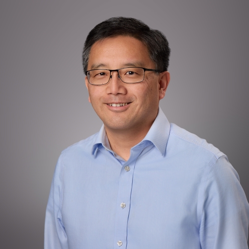 Headshot of male with short black hair with eyeglasses wearing a light blue button down shirt