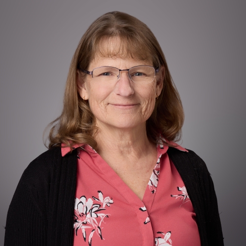 Headshot of female with eyeglasses wearing a red patterned blouse under a black sweater.
