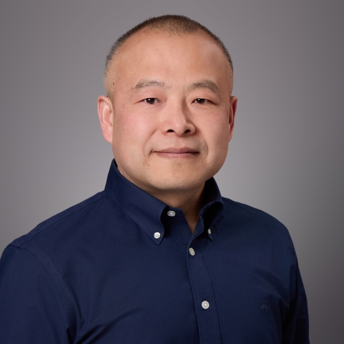 Headshot of male with very short hair wearing a blue button down shirt.
