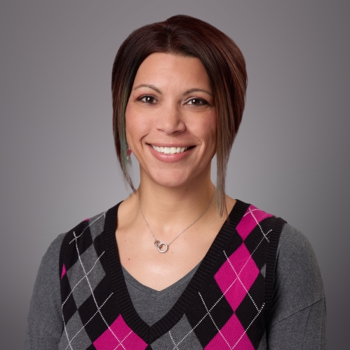 Headshot of female with short brown hair wearing an argyle vest in grey, pink, and black.