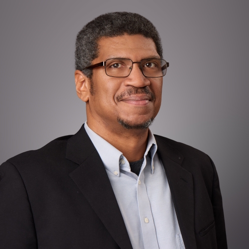Headshot of Black male with eyeglasses wearing a light button down shirt and a black suit jacket.