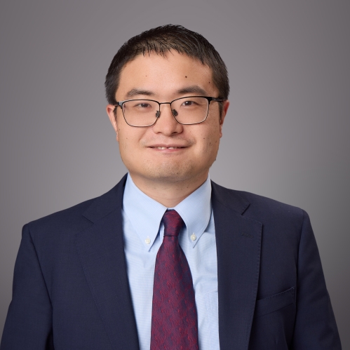 Headshot of male with eyeglasses and short hair wearing a blue jacket, light blue button down shirt and a burgundy tie.