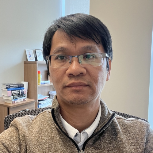 Headshot of Asian male with short black hair wearing eyeglasses and a tan colored zip up top.