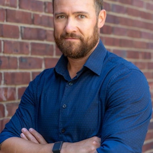 Headshot of male wearing blue shirt, with folded arms.