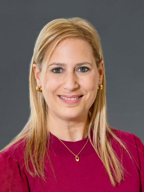 Head shot of woman with long blond hair, wearing gold hoop earrings, a gold necklace, and a red pullover sweater.