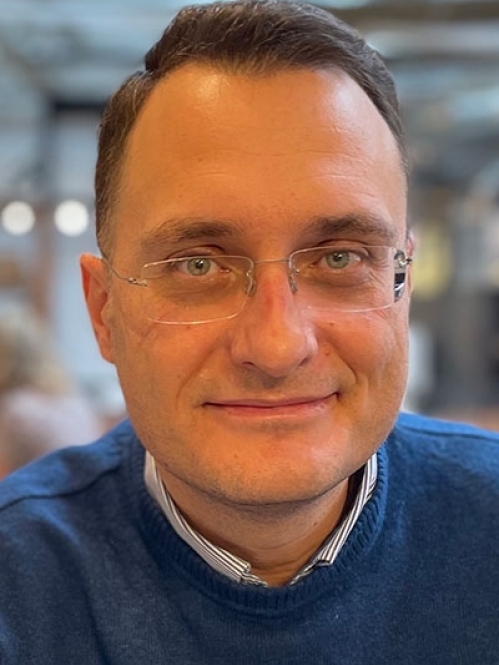 Head shot of male with short brown hair and eyeglasses, wearing a blue pullover sweater.
