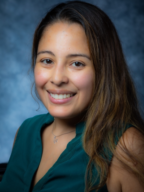 Head shot of female with ong brown hair, wearing a dark green top.