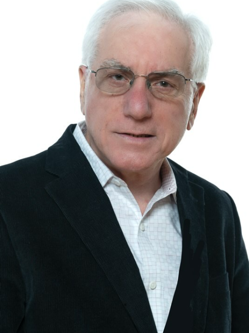 Male with shortwhite hair, and eyeglasses, wearing a black suit jacket and white button down shirt.