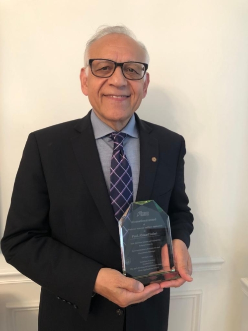 Male with white hair and eyeglasses holds award.