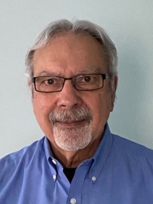 Headshot of male with short, white hair, and facial hair, wearing eyeglasses and a button down blue shirt.