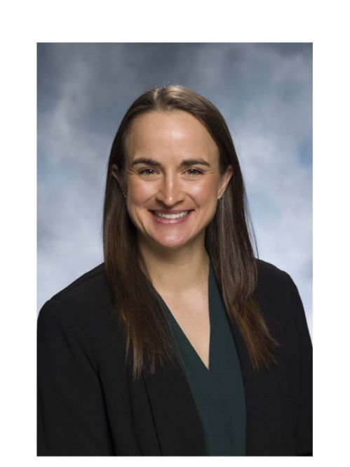Headshot of female with long brown hair wearing a black suit jacket and dark green shirt.
