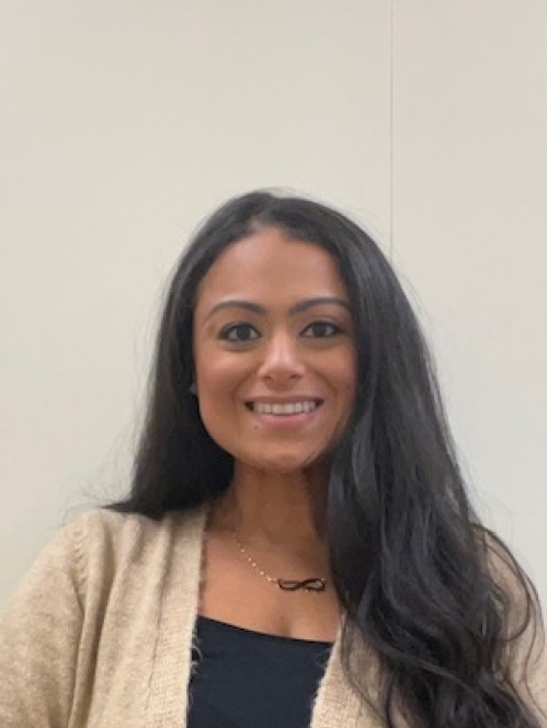 Headshot of female with long black hair, wearing a tan sweater and a black shirt. an 