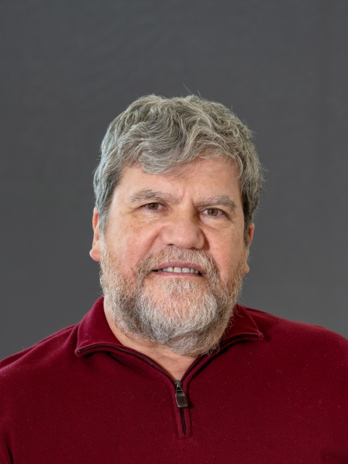 Headshot of male with short, grey hair and facial hair, wearing a burgundy half-zip sweater.