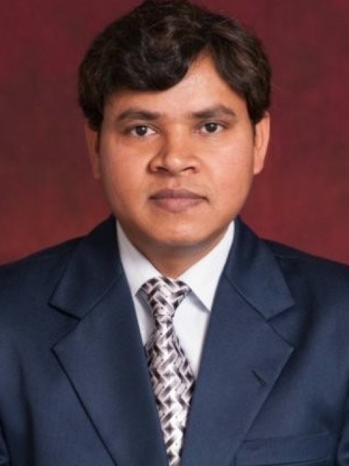 Headshot of male with dark hair, weasring a blue suit, shite shirt, and silver patterned tie.