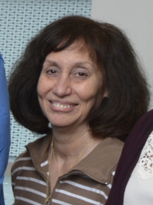 Head shot of woman with brown shoulder length curly hair, wearing a stripped white and brown shirt.