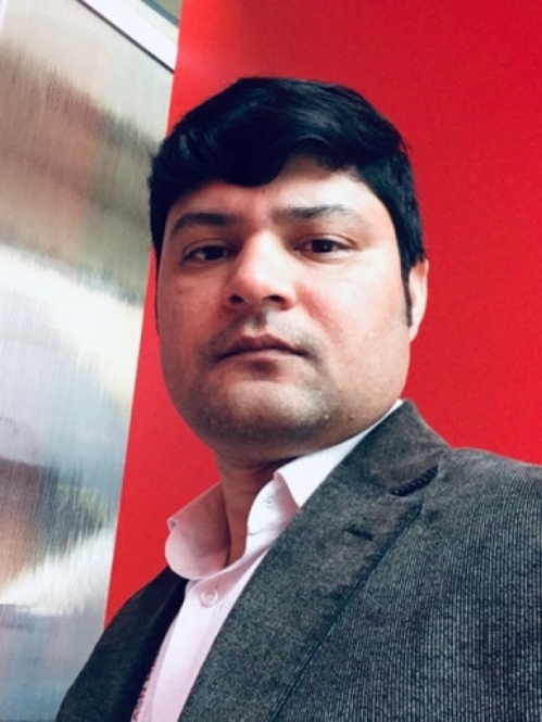 Head shot of male with dark short hair, wearing a pink button down shirt with a grey suit jacket.