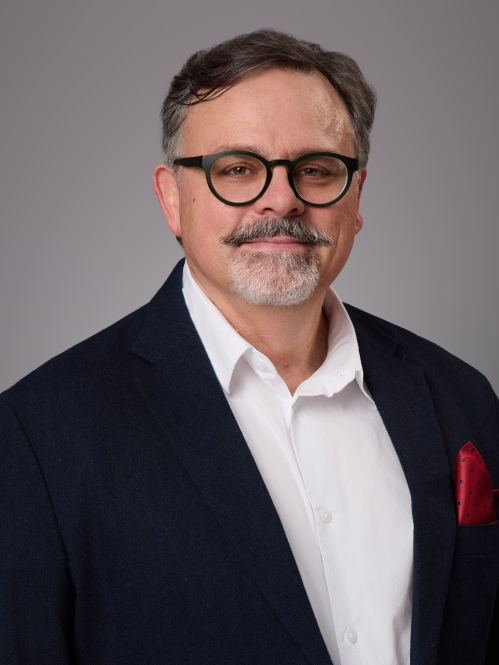 Headshot of male with eyeglasses wearing a white button down shirt a black suit jacket and a red pocket square