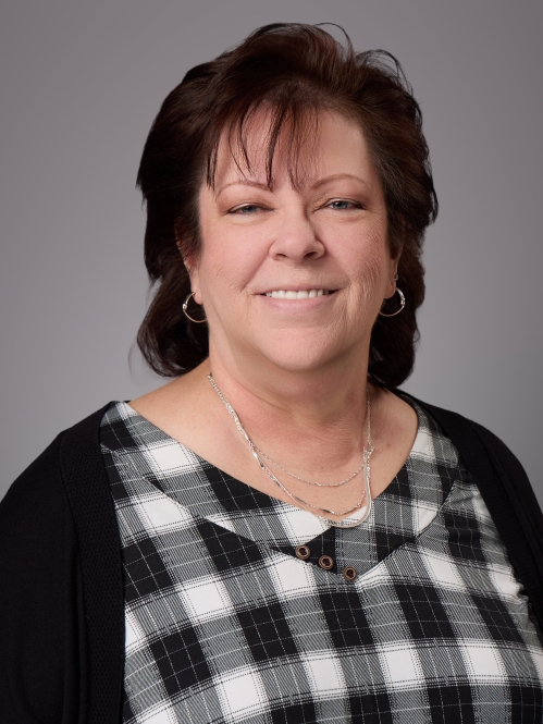Headhsot  of woman with short brown hair wearing a black and white checkered blouse underneath a black sweater.