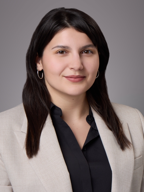 Headshot of female with long black hair, wearing a black blouse beneath a tan jacket.