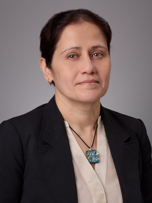Headshot of female with brown hair pulled back wearing a tan blouse, black jacket and a necklace.