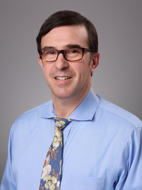 Headshot of male with short brownhair and eyeglasses, wearing and light blue shirt and patterned blue tie.