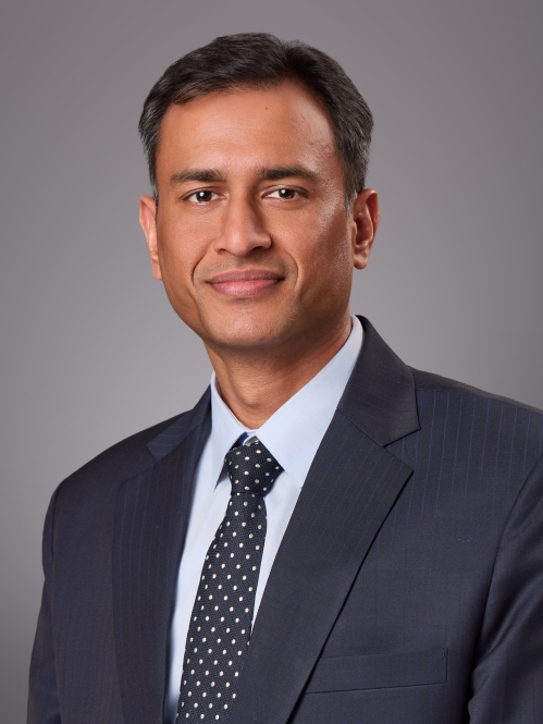 Headshot of male wearing a dark blue suit, light blue shirt, and dark blue tie.