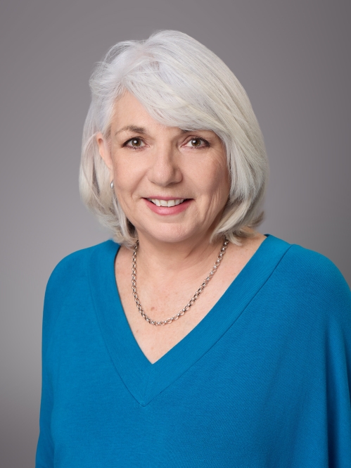 Headshot of woman with grey hair and a v neck blue pullover.