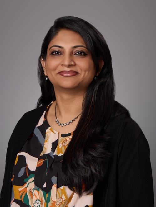 Headshot of female with long black hair wearing a patterned blouse, a black jacket and a necklace.