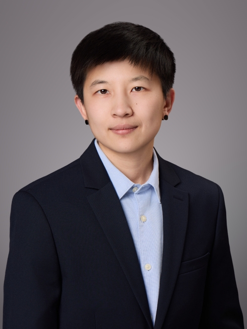 Headshot of woman with short black hair, wearing black post earrings, a light blue button shirt and a dark blue jacket.