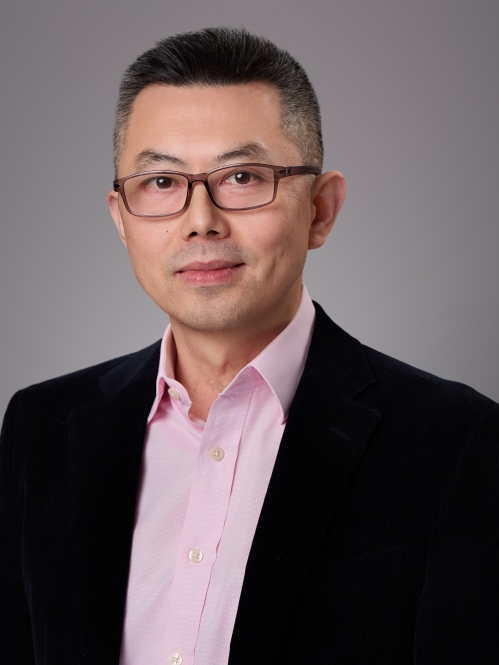 Headshot of male with eyeglasses wearing a pink button down shirt and a black suit jacket.