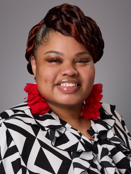 Headshot of black woman with long red earrings wearing a black and white patterned shirt.