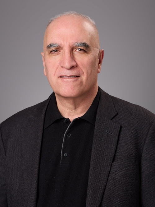 Headshot of male with white hair wearing a black sweater underneath a black suit jacket.