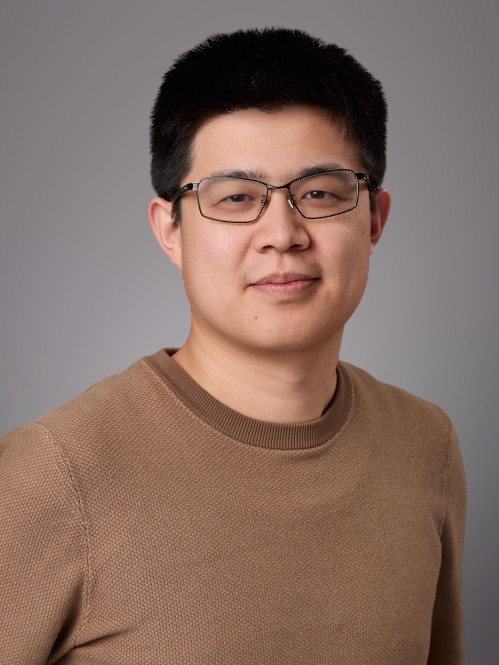 Headshot of male with short black hair and eyeglasses wearing a brown sweater.