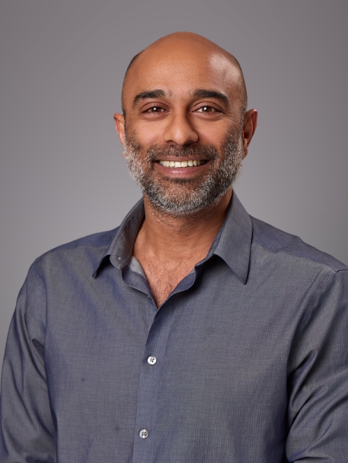 Headshot of bald male with sruffy beard wearing a bluish grey button down shirt.