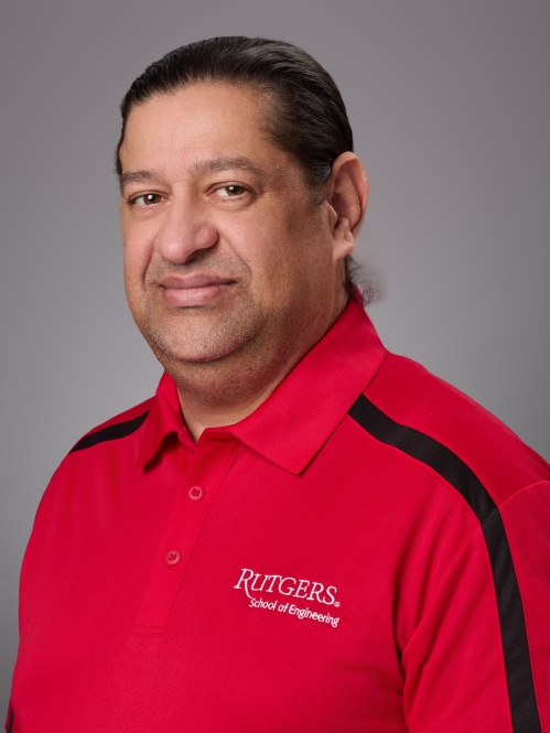 Headshot of male with dark brown hair pulled into a ponytail wearing a red Rutgers polo shirt.