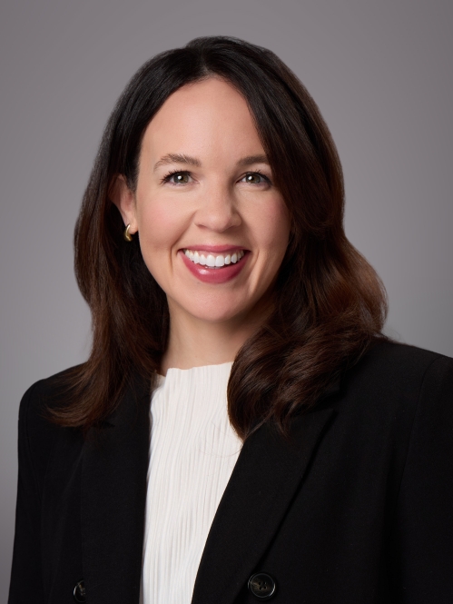 Headshot of wman with long brown hair wearing a beige blouse under a black suit jacket.