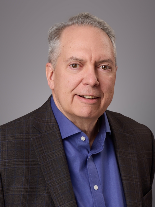 Headsot of male with grey hair wearing adark blue button down shirt and a black suit jacket.