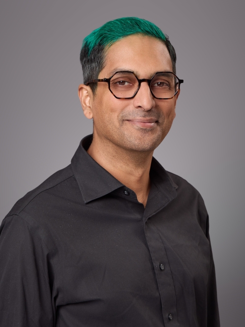 Headshot of male with eyeglasses and green hair wearing a black button down shirt