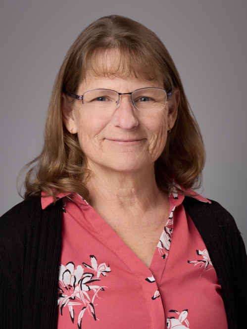 Headshot of female with eyeglasses wearing a red patterned blouse under a black sweater.