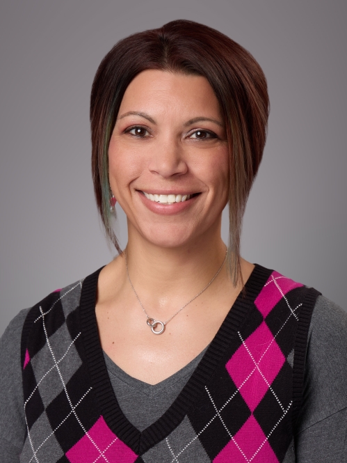 Headshot of female with short brown hair wearing an argyle vest in grey, pink, and black.