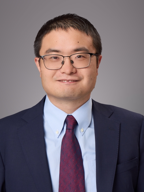 Headshot of male with eyeglasses and short hair wearing a blue jacket, light blue button down shirt and a burgundy tie.