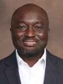 headshot of smiling black man with short beard wearing a black suit jacket and white button down collared shirt