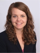 Headshot of female with long, wavy, light hair, wearing a black suit jacket.