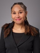 Headshot of black woman with long hair wearing big gold hoop earrings, a black blouse underneath a black jacket.