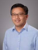 Headshot of male with short black hair with eyeglasses wearing a light blue button down shirt