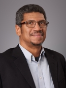 Headshot of Black male with eyeglasses wearing a light button down shirt and a black suit jacket.