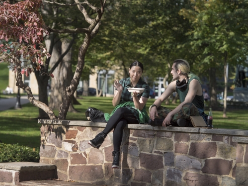 Two students eat lunch on the wall of the Red Lion Bench on Voorhees Mall on the College Ave campus