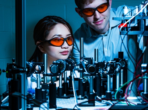 Student and professor both wearing eye protection look at lasers.