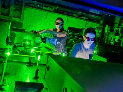 Two students wearing goggles in a lab with lasers